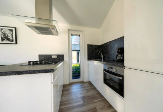 Moderne Küche in einer Lodge mit weißen Schränken, schwarzer Arbeitsfläche und großem Fenster.
