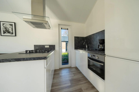 Moderne keuken in een lodge met witte kasten, zwart aanrechtblad, oven, gaskookplaat en groot raam.