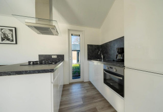Cucina moderna in una lodge con mobili bianchi, piano nero, forno, piano a gas e ampia finestra.