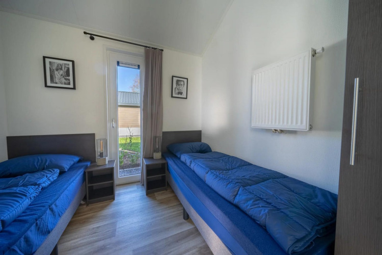 Bright lodge room with two single beds, blue bedding, a glass door, and garden view outside.