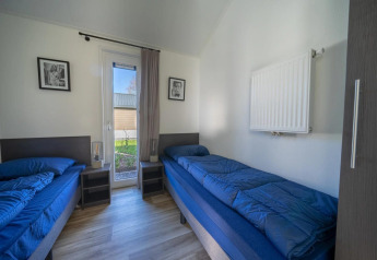 Luminoso cuarto en lodge con dos camas individuales, ropa de cama azul y puerta al jardín.