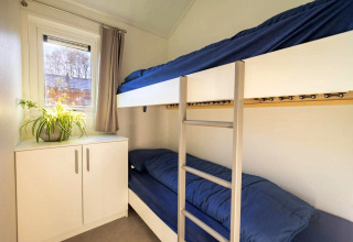 Gemütliches Zimmer in einer Lodge mit Etagenbetten, blauer Bettwäsche, Schrank und Fenster.