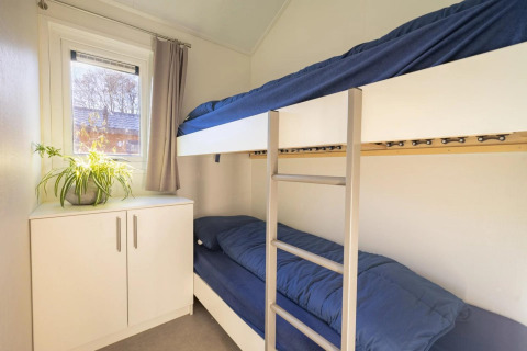 Chambre confortable de lodge avec lits superposés, literie bleue, armoire blanche et plante verte.