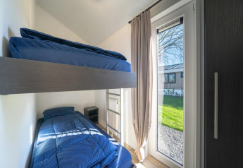 Moderne lodgekamer met stapelbedden, blauwe dekens, grote raam en zicht op het buitengroen.