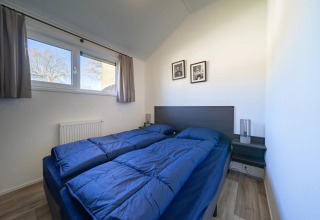 Chambre moderne dans un lodge avec deux lits simples, couettes bleues et vue extérieure par la fenêtre.