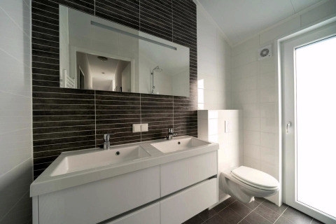 Modernes Badezimmer mit Doppelwaschbecken, großem Spiegel, Wandtoilette und viel Tageslicht.