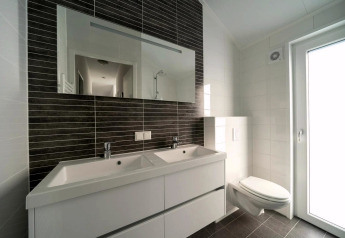 Bagno moderno con doppio lavabo, grande specchio, wc sospeso e molta luce naturale dalla porta.