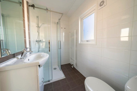 Modernes Badezimmer in einer Lodge mit Glasdusche, weißem Waschbecken, Fenster, Heizkörper und WC.