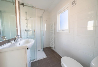 Baño moderno de lodge con cabina de ducha de cristal, lavabo blanco, ventana, radiador y un inodoro.