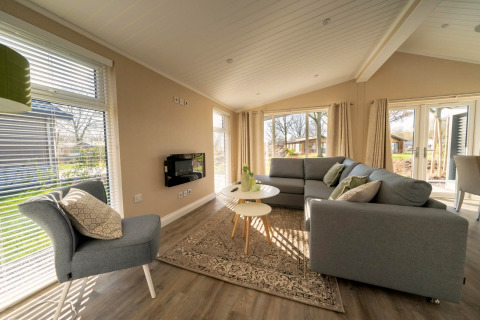 Lichte, moderne woonkamer in een lodge met grote ramen, grijze banken en uitzicht op buiten.