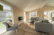 Bright, modern living room in a lodge with large windows, grey couches, and views of the outdoors.