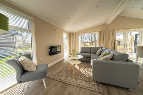 Salón luminoso y moderno en una cabaña con grandes ventanales, sofás grises y vistas al exterior.