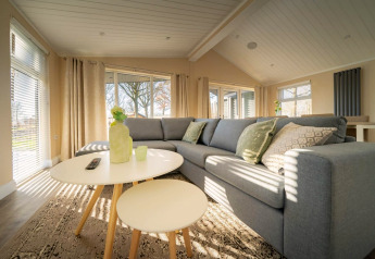 Soggiorno di lodge moderno con divano angolare grigio, tavolini rotondi e grandi finestre luminose.
