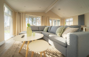 Modern lodge living room with a grey corner sofa, round tables, large windows and sunlight streaming in.