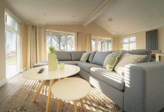 Soggiorno di lodge moderno con divano angolare grigio, tavolini rotondi e grandi finestre luminose.