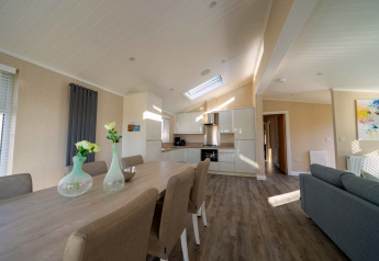 Interno lodge moderno con cucina open space, tavolo da pranzo, sedie eleganti e ampio soggiorno luminoso.