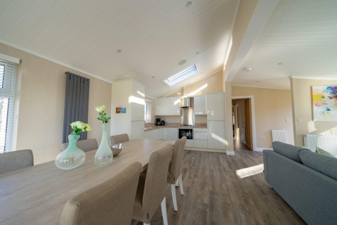 Interior de lodge moderno con cocina abierta, mesa de comedor, sillas elegantes y salón luminoso.