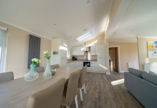 Interno lodge moderno con cucina open space, tavolo da pranzo, sedie eleganti e ampio soggiorno luminoso.