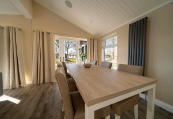 Sala da pranzo in un lodge con tavolo in legno chiaro, sei sedie e grandi finestre dalle tende beige.