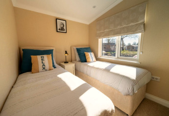Helles Schlafzimmer in einer Lodge mit zwei Einzelbetten, blauen Kissen und Fenster mit Gartenblick.