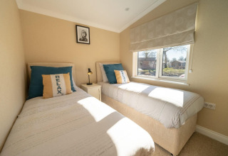 Dormitorio luminoso en una cabaña con dos camas individuales, cojines azules y ventana soleada al exterior.