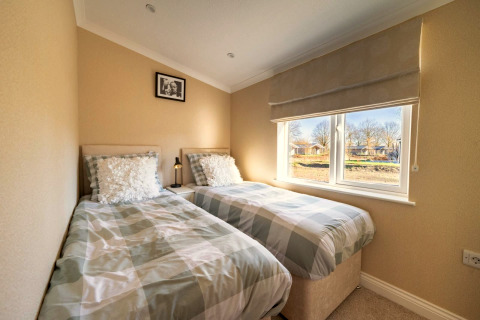 Chambre lumineuse de lodge avec deux lits simples, grande fenêtre et murs beiges, décoration épurée.