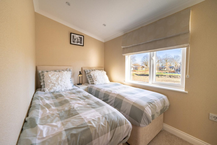A bright lodge bedroom featuring two single beds, large window, plaid bedding, and beige painted walls.