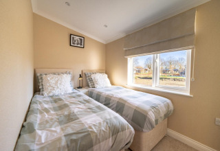 Lichte lodge slaapkamer met twee eenpersoonsbedden, grote ramen en een neutraal kleurenschema.