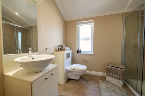 Modern lodgebadkamer met hangend toilet, glazen douche, witte wastafel en een rieten wasmand op de vloer.