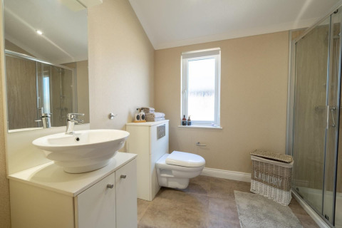 Moderne lodgebadkamer met zwevend toilet, glazen douche, waskom en een witte rieten wasmand op de vloer.