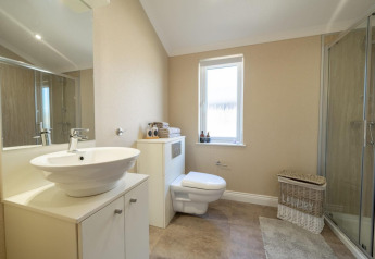 Moderne lodgebadkamer met zwevend toilet, glazen douche, waskom en een witte rieten wasmand op de vloer.