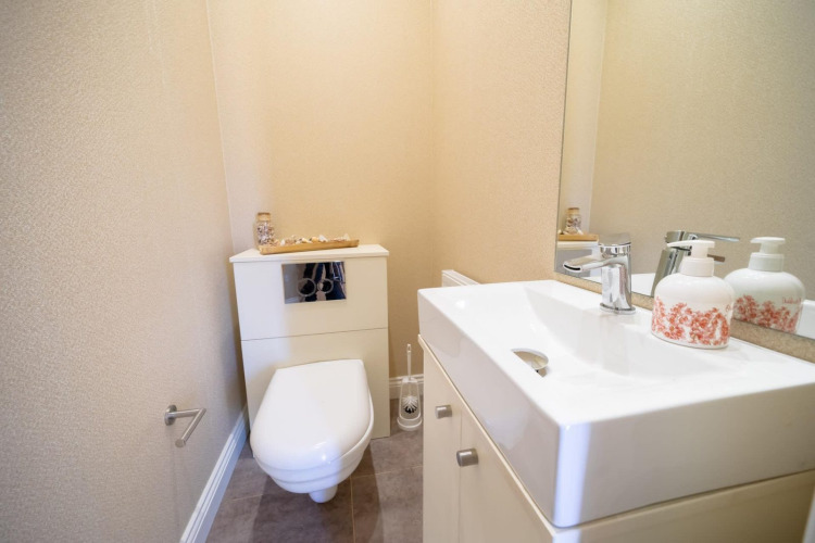 Photo of a modern, small restroom at a lodge featuring a wall-mounted toilet, sink, and large mirror.