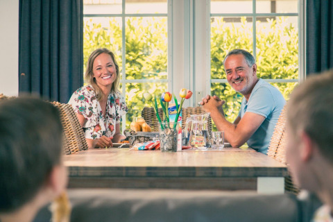 Een gezin geniet samen van een maaltijd in een glampingverblijf en lacht rond een houten tafel.