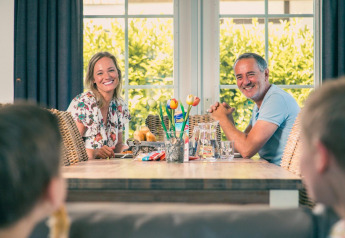 Una famiglia si gode un pasto insieme in una sistemazione glamping, sorridendo attorno a un tavolo di legno.