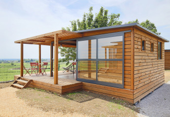 Moderna cabina di legno Chalet Evasion Vista Vue Vignes con parete in vetro e terrazza su campi verdi.