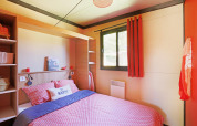 Gezellige slaapkamer met rood beddengoed, groot raam en ‘be happy’ kussen bij Chalet Evasion Vista Vue Vignes.