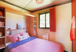 Knusse slaapkamer met rood beddengoed, groot raam en 'be happy' kussen in Chalet Evasion Vista Vue Vignes.