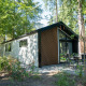 Moderne Berkel 4 lodge i skovmiljø med havemøbler og store vinduer, omgivet af grønne træer og buske.