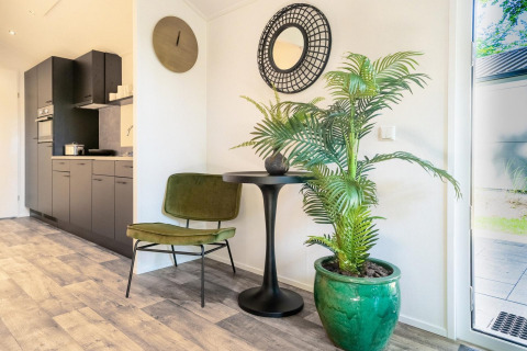 Modern lodge-interieur met groene stoel, zwarte tafel, grote plant en keuken bij De Utrechtse Heuvelrug.