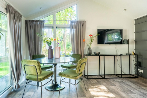 Lichte eetkamer met ronde tafel, groene stoelen en tv in lodge Berkel 4 op De Utrechtse Heuvelrug, Nederland.