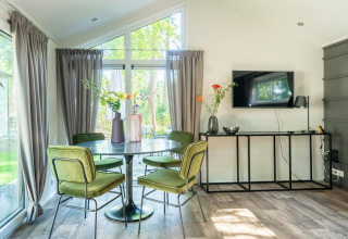 Luminoso comedor con mesa redonda, sillas verdes y televisor en una cabaña en De Utrechtse Heuvelrug, Países Bajos.