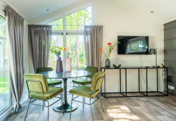 Luminoso comedor con mesa redonda, sillas verdes y televisor en una cabaña en De Utrechtse Heuvelrug, Países Bajos.