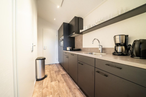 Moderne zwarte keuken met koffiezetapparaat en prullenbak bij Berkel 4, De Utrechtse Heuvelrug, Nederland.