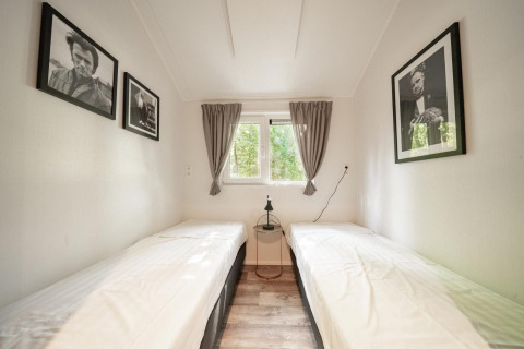 Minimalistische kamer met twee eenpersoonsbedden, zwart-wit portretten en uitzicht op bomen buiten.