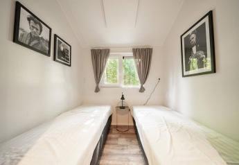 Habitación minimalista con dos camas individuales, cuadros en blanco y negro y vista a árboles fuera.