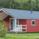 Rød Boslodge 4 med gråtag og hvid terrasse i grønne omgivelser, omgivet af træer og natur.
