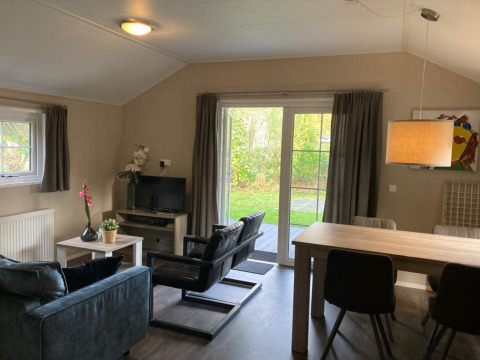 Stue i Boslodge 4 ved De Utrechtse Heuvelrug, Nederlandene, med moderne møbler, tv og udsigt til have.