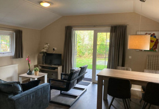 Stue i Boslodge 4 ved De Utrechtse Heuvelrug, Nederlandene, med moderne møbler, tv og udsigt til have.