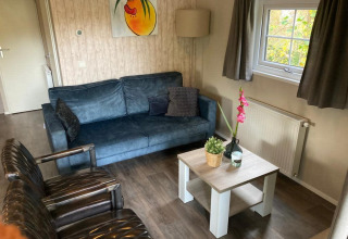 Wohnzimmer in Boslodge 4 auf De Utrechtse Heuvelrug, Niederlande, mit blauer Couch, Stühlen und Couchtisch.
