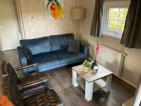 Stue i Boslodge 4 på De Utrechtse Heuvelrug, Holland, med blå sofa, lænestole og et lille sofabord.